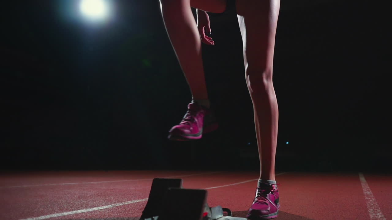 Female hispanic athlete training at running track in the dark. Slow motion
