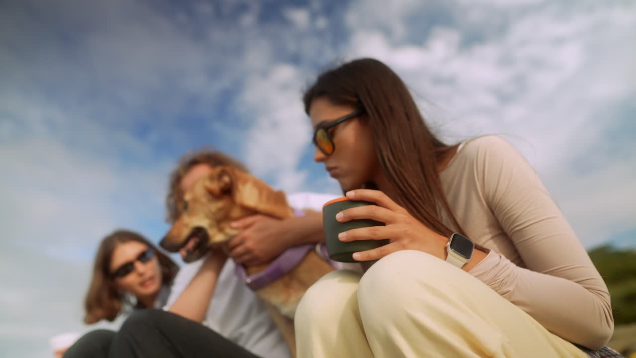 Amici con cane che si rilassano all'aperto e versano una bevanda calda