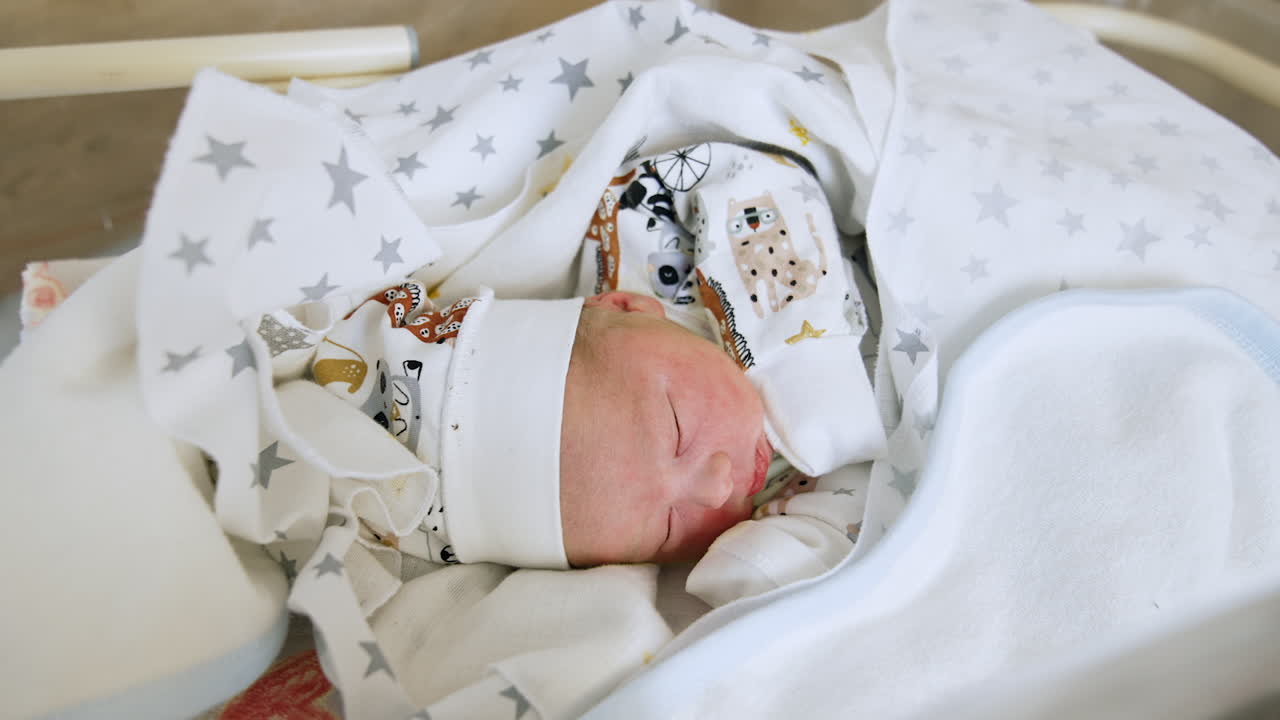 Overhead view of a newborn infant lying in the sheets. Cute little baby in cap and shirt sleeps peacefully.