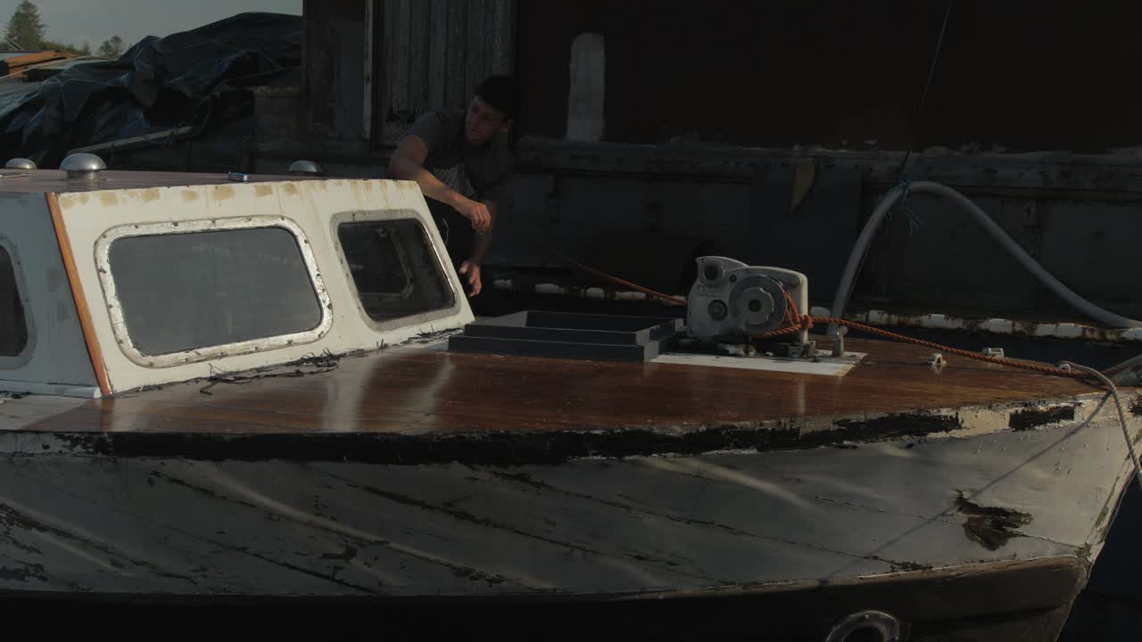 목선의 뱃머리에 물 잔물결이 반사되고, 청년 복원 작업