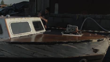 Wellen-Des-Wassers-Spiegeln-Sich-Auf-Dem-Bug-Eines-Holzbootes,-Restaurierungsarbeiten-Eines-Jungen-Mannes