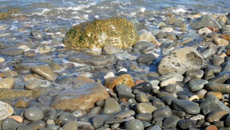 Sunny-blue-ocean-tide-washing-over-colourful-stone-pebble-beach-holiday-scene-dolly-right