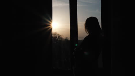 the silhouette of a lonely woman sitting on the window sill and looking out the window