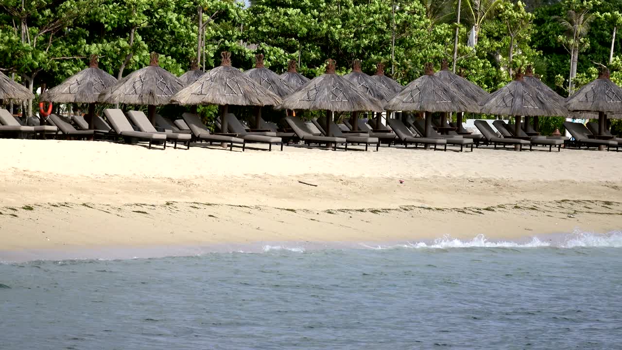 las olas del mar cálido corren en la playa de arena del complejo tropical con sombrillas y sillones