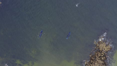 perspectiva de drones de arriba hacia abajo de barcos de currach luchando contra la corriente para remar hacia el mar