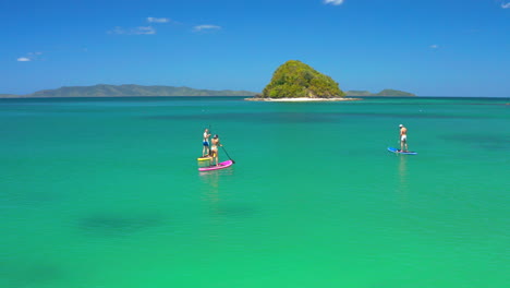 people paddleboarding in turquoise tropical waters with lush islands