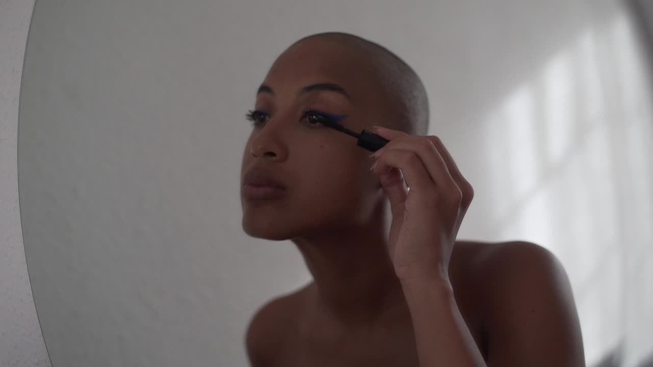 Serious black woman applying mascara on eyelashes