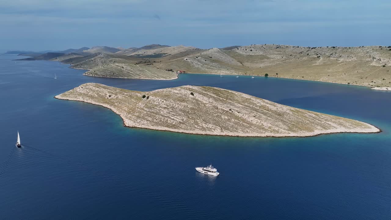 Aerial Kornati island with rocky sloping shoreline and deep blue waters under clear skies, yachts and sppedboats anchored offshore