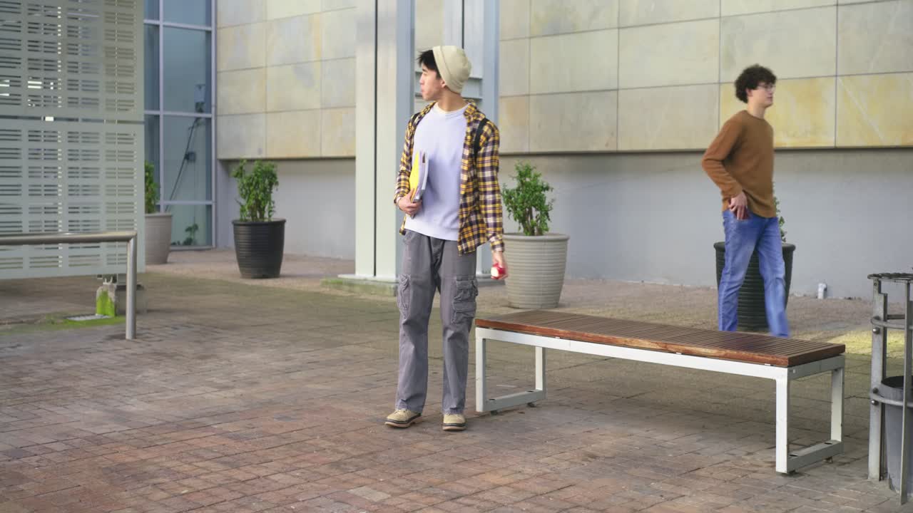 Asian man entering left carrying yellow folder, red can, pausing near bench, preparing to leave
