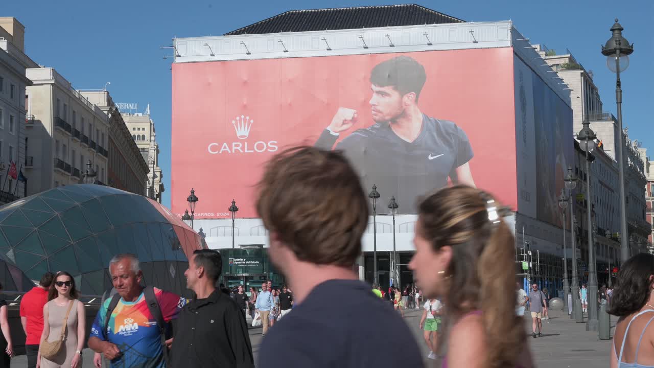 Large billboard featuring Carlos Alcaraz in a busy Madrid city square