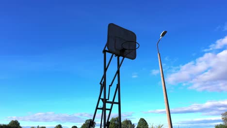 Silhouette-of-old-basketball-hoop-against-blue-sky,-low-angle-orbit