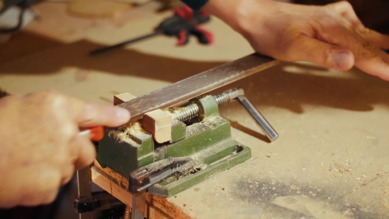 Close-up of a craftsman using a metal file to shape and smooth a wooden piece clamped in a vise. Authentic DIY woodworking footage for craft, carpentry and maker projects