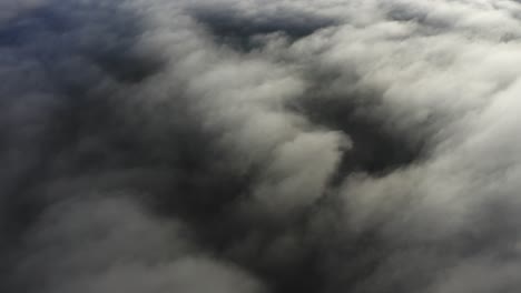 flying over bright white clouds and dark mysterious land in shadow below