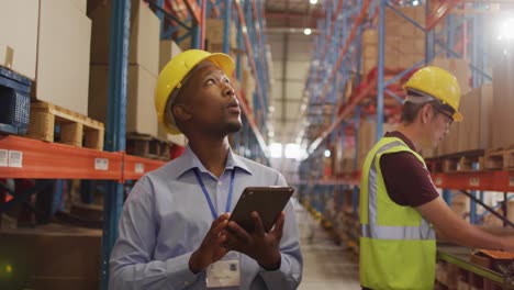 African american male worker with helmet using tablet in warehouse