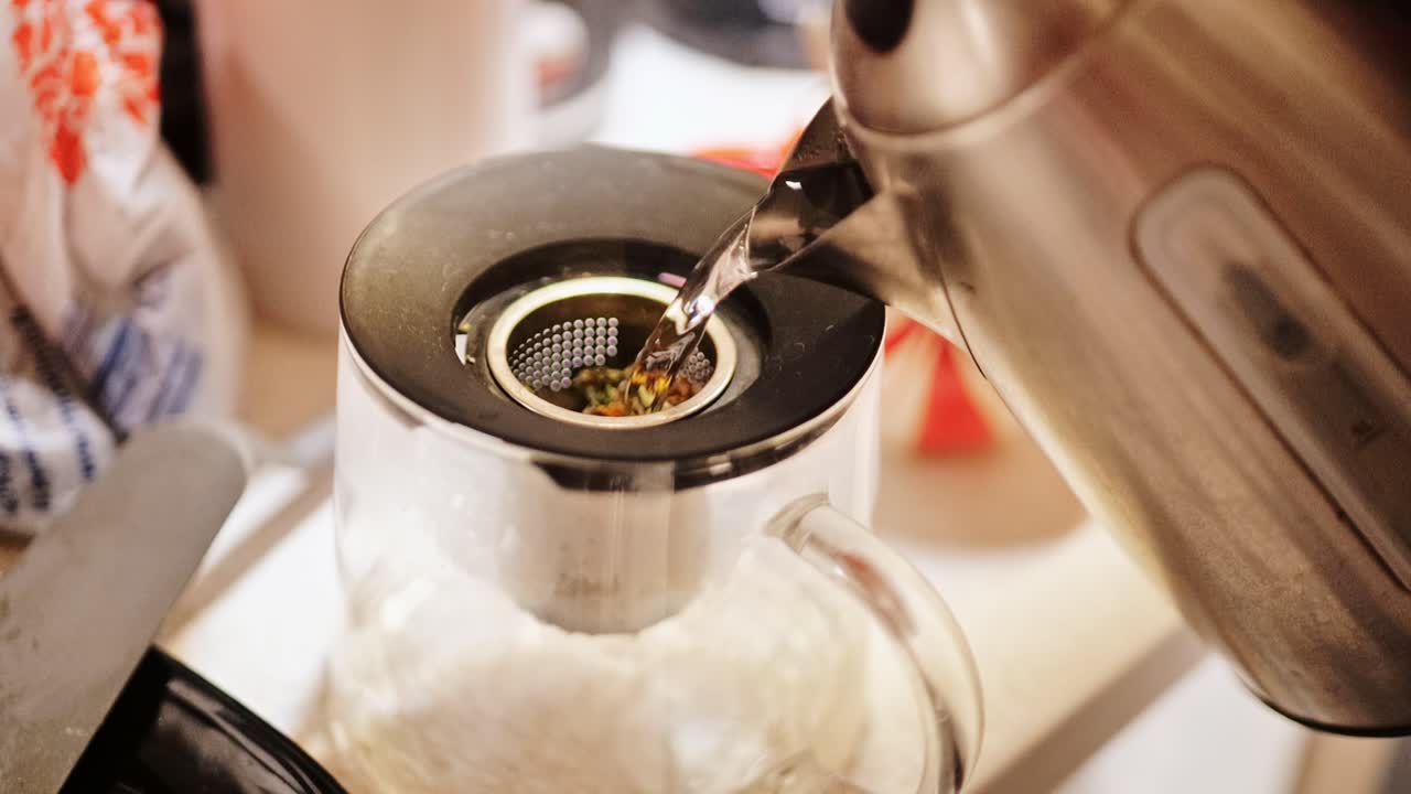 Close up of hot tea stream filling transparent teapot in warm kitchen light