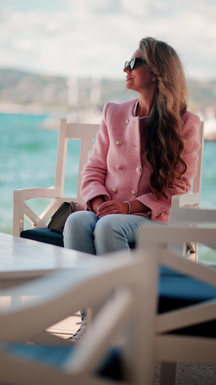 Woman in a pink blazer sitting on a chair at the beach in Antibes, France. Vertical