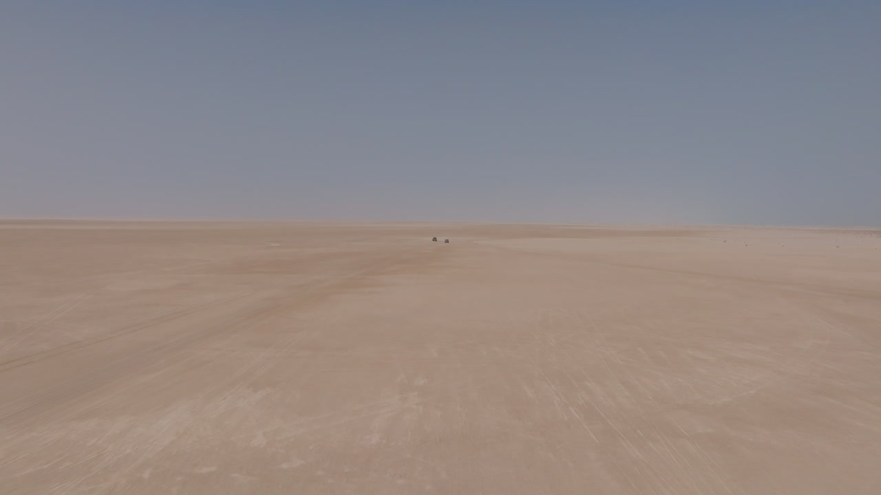 Two cars driving through vast desert plains toward Bar Al Hikman, Oman