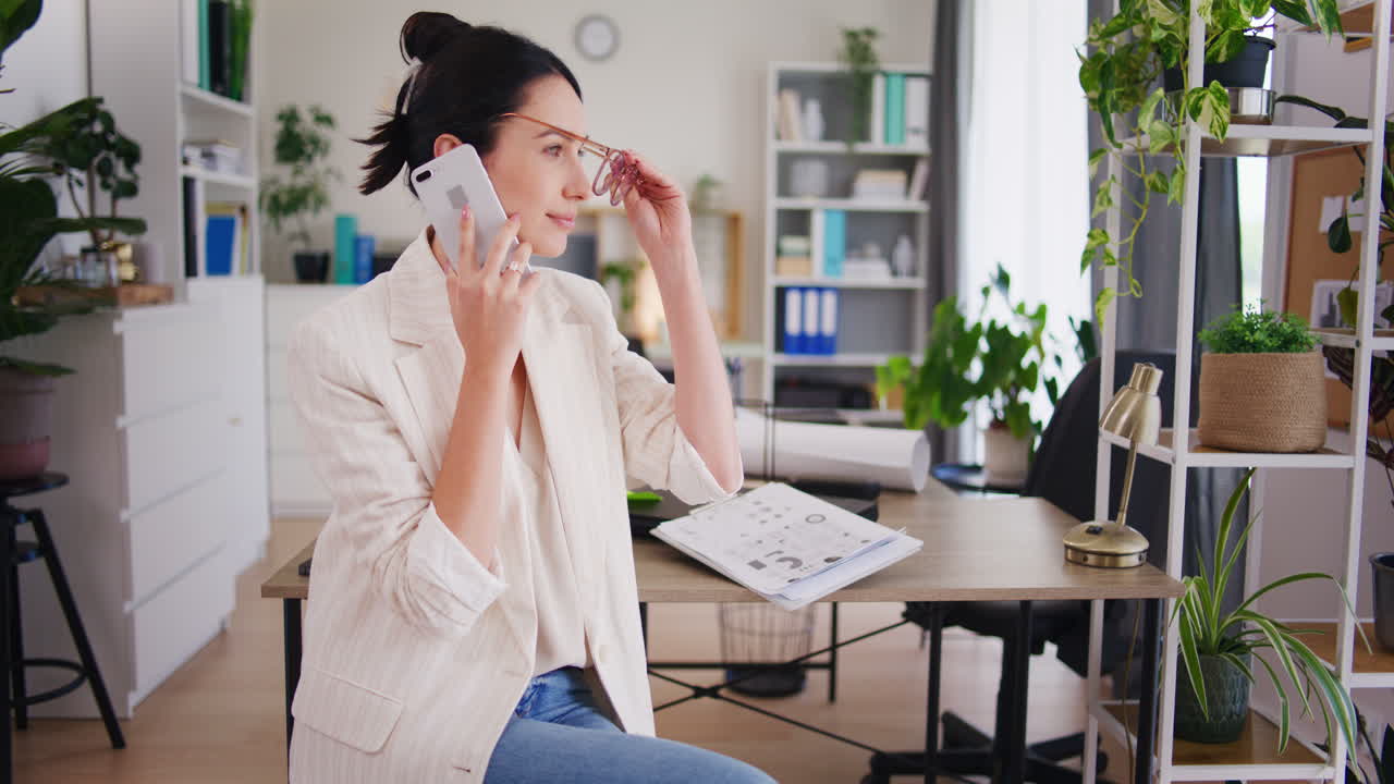 Glad og eftertænksom kvinde taler i mobiltelefon på kontoret