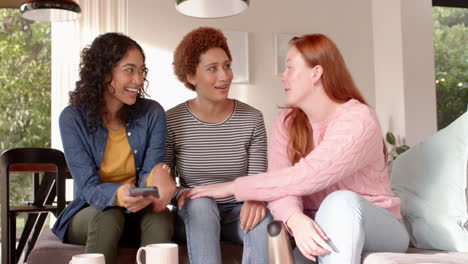 laughing and chatting, diverse female friends hanging out on couch with smartphone