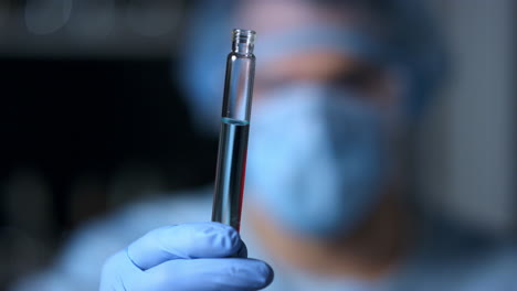 Macro-video-of-doctor-holding-test-tube-in-blue-gloved-hands.Protective-mask.