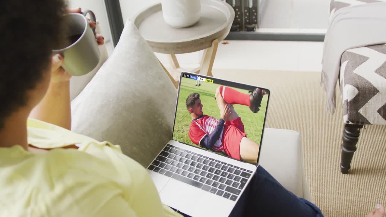 Donna afroamericana che usa un laptop con diversi calciatori uomini che giocano una partita sullo schermo