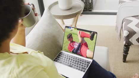 mujer afroamericana usando una computadora portátil con varios jugadores de fútbol masculino jugando un partido en la pantalla