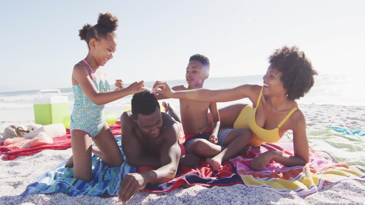Famiglia afroamericana sorridente distesa sugli asciugamani su una spiaggia assolata.