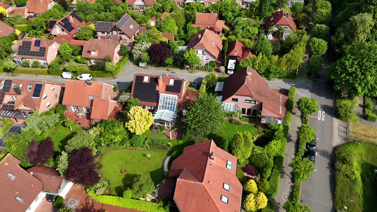 Solar panels of single family houses in german neighborhood. Orange red tiles on roof of homes. Green garden and trees in spring. Sunny day in quiet suburb city. Aerial top down.