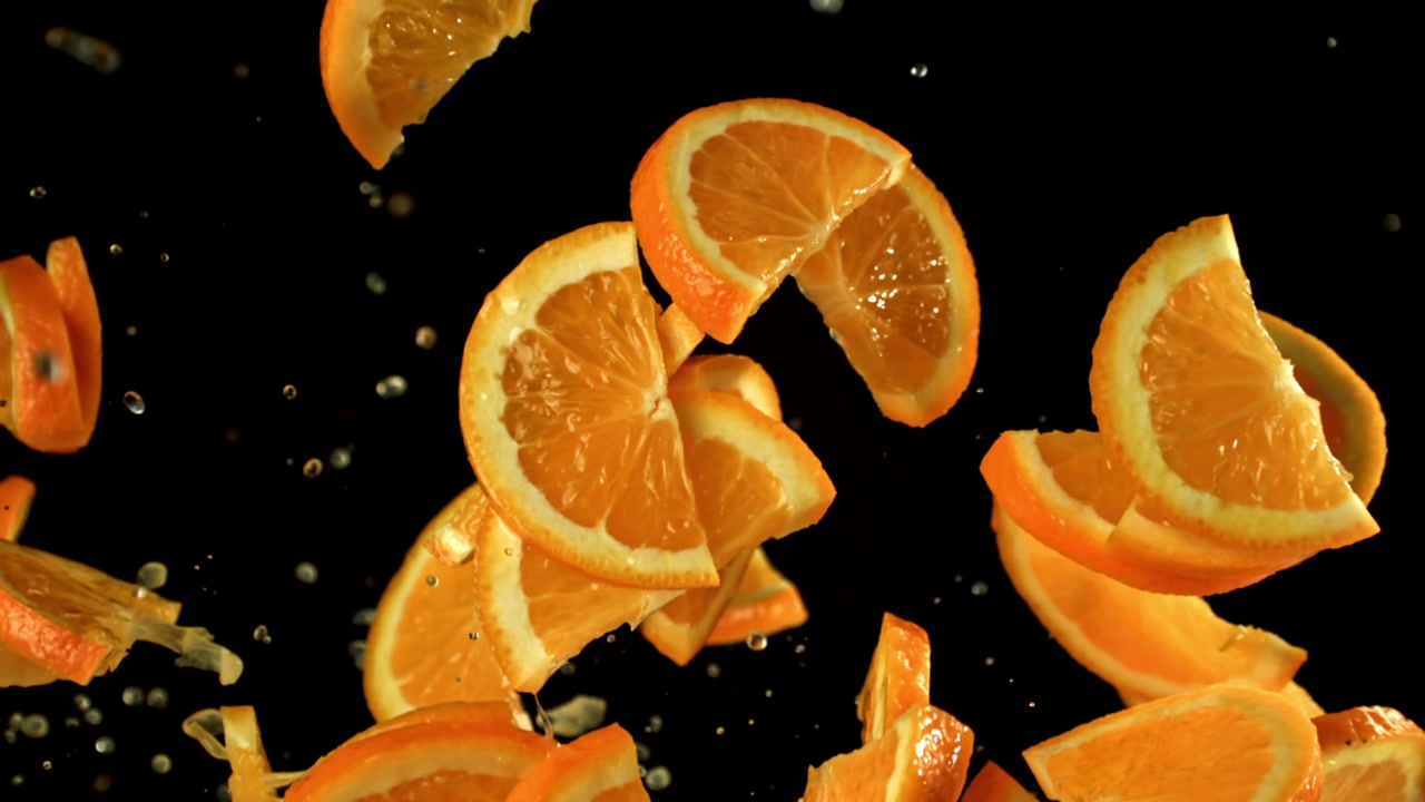 Frische Orangenscheiben und Schalen fallen mit Wasserspritzern auf schwarzem Hintergrund