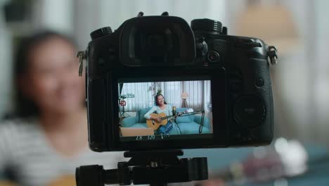 close up de un monitor de cámara grabando a una mujer asiática sosteniendo una guitarra y sonriendo mientras transmite en vivo por una computadora portátil en casa