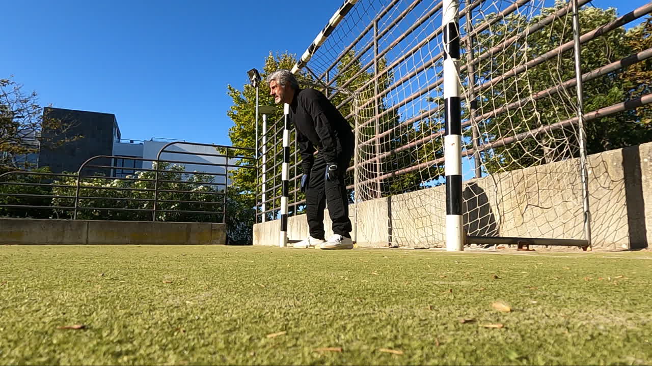 야외에서 축구를 하면서 골키퍼를 방어하고 공을 잡는 집중된 시니어 골키퍼