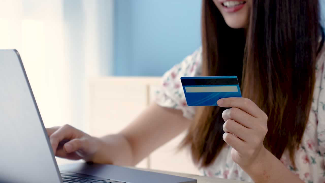 4k 50fps, hermosa chica asiática, hermosa muchacha asiática, con una camisa blanca floral, está pagando en línea por un pedido a través de una computadora portátil, con una tarjeta de crédito en la mano, compras en línea.