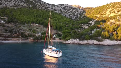 drone descending in a cove with view on a sailboat and island at sundown in croatia