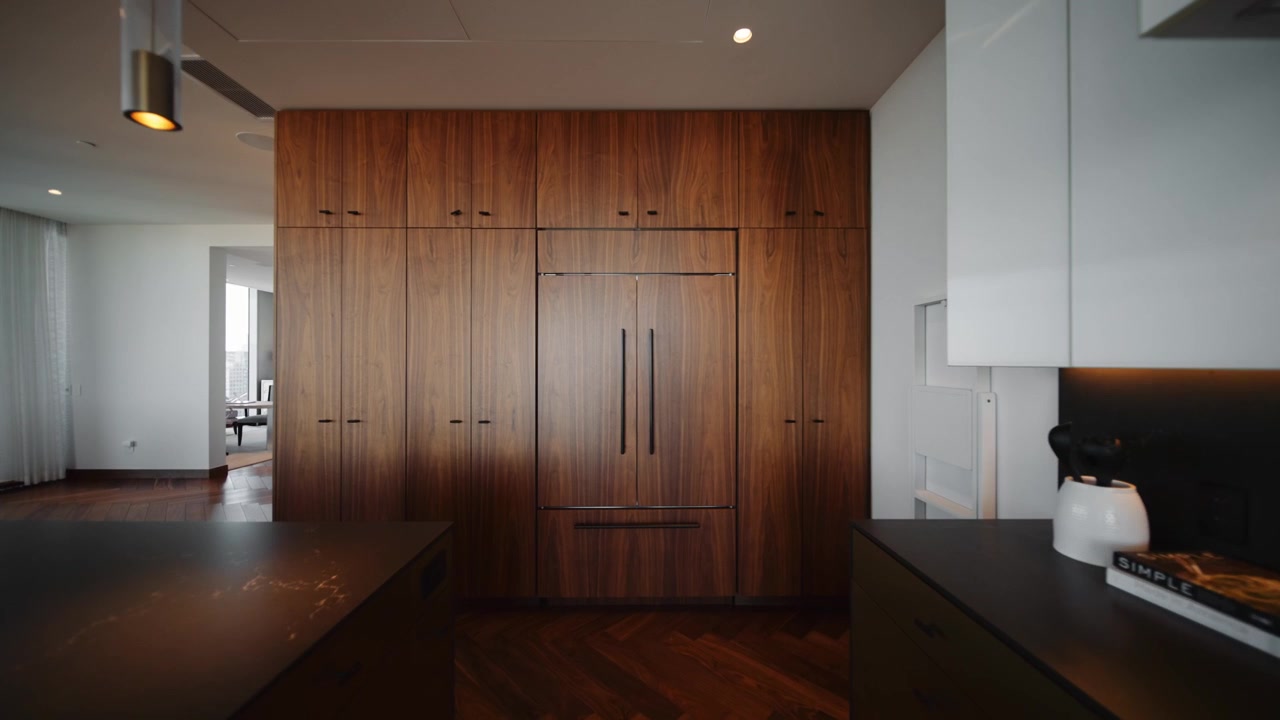 Elegant, moderne kjøkken med en svart kjøkkenøy, treinnredning og integrerte hvitevarer i en luksusleilighet, med minimalistisk design og eksklusive overflater for en raffinert livsstil.