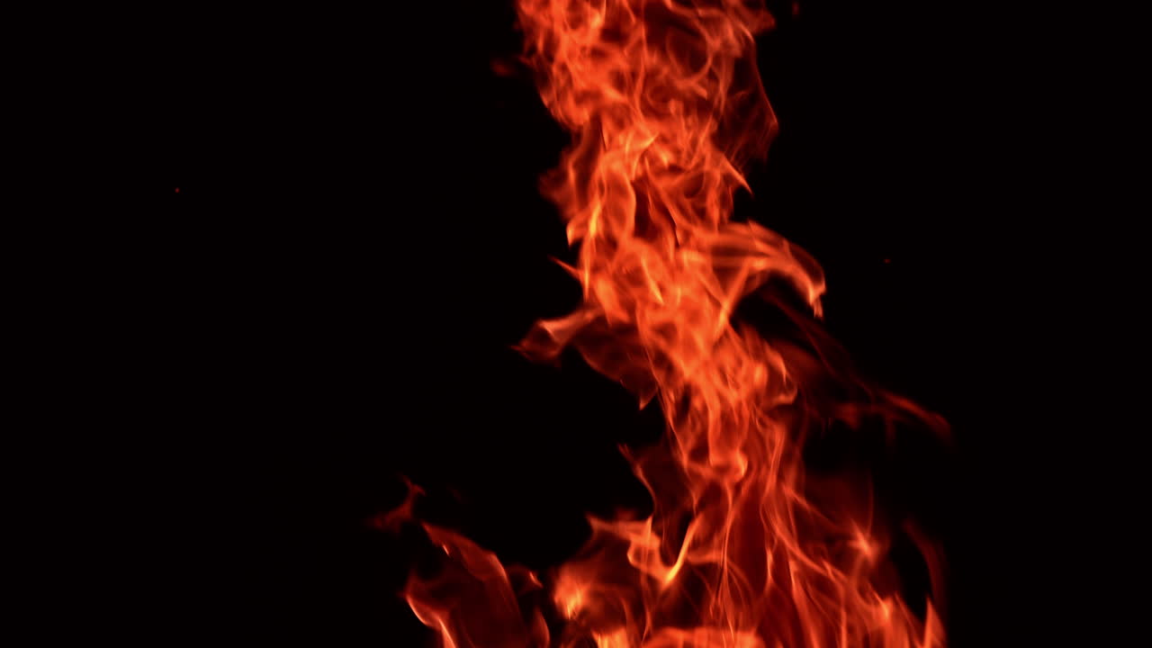 Red tongues of flame moving in the darkness. Hot blaze isolated with sparkles flying up. Close up.