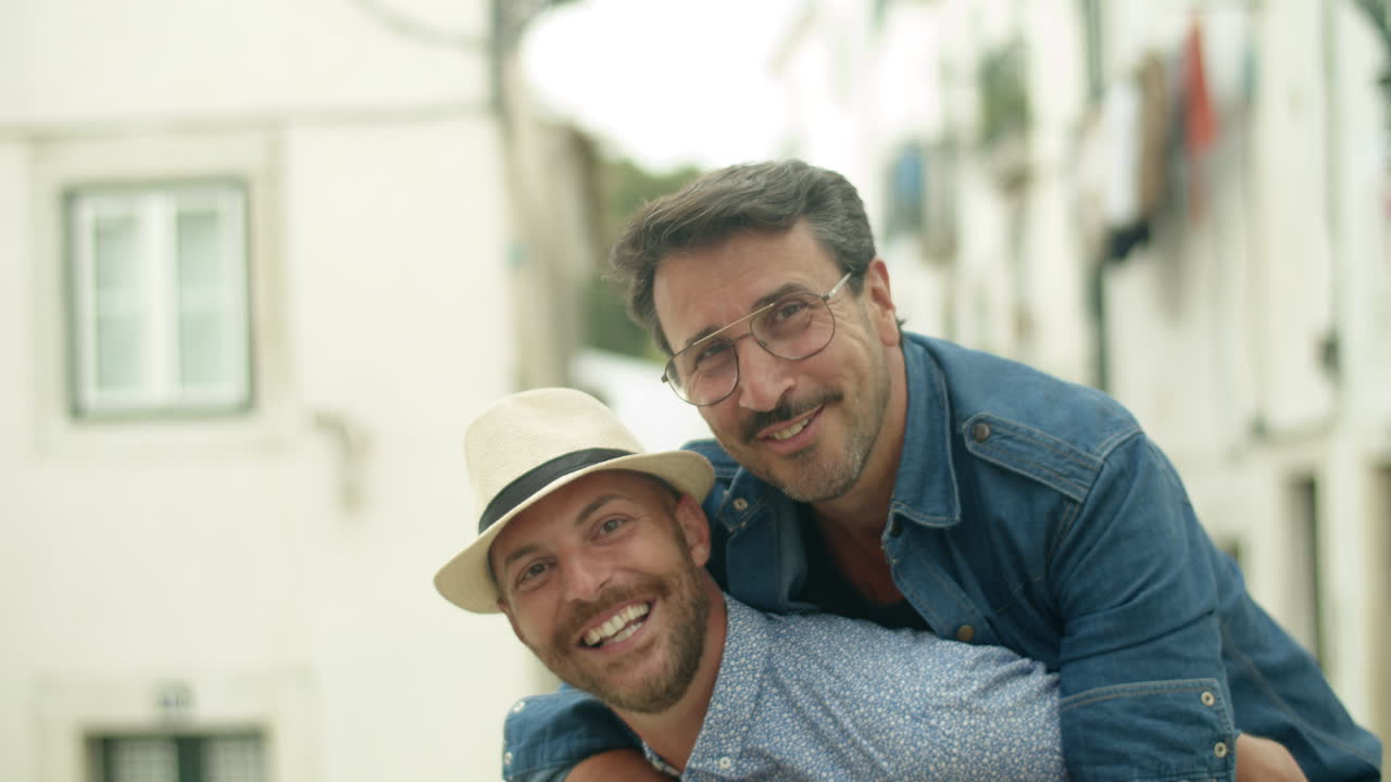 Hombre homosexual feliz sentado a la espalda de su novio al aire libre.