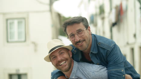 happy homosexual man sitting on his boyfriend's back outdoor