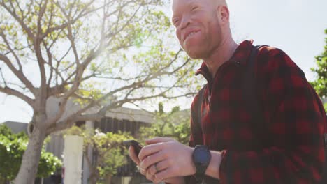 hombre afroamericano albino feliz con rastas usando un teléfono inteligente