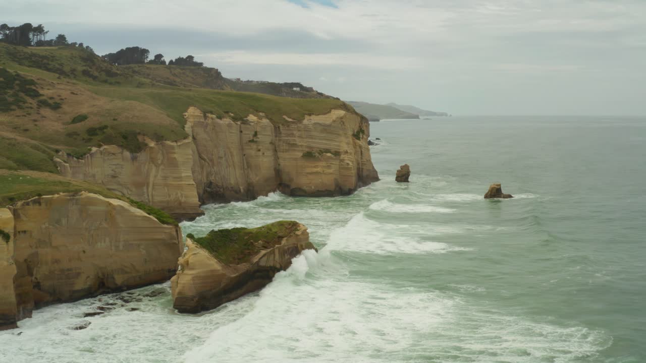 Aerial panning left to right shot of islet cliff rock formations along the coast in New Zealand