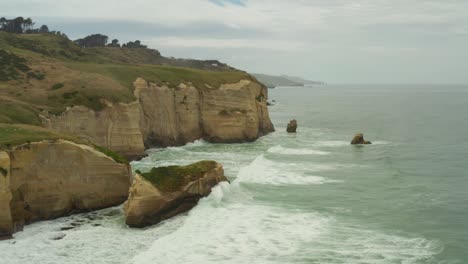 Toma-Panorámica-Aérea-De-Izquierda-A-Derecha-De-Formaciones-Rocosas-De-Acantilados-De-Islotes-A-Lo-Largo-De-La-Costa-En-Nueva-Zelanda