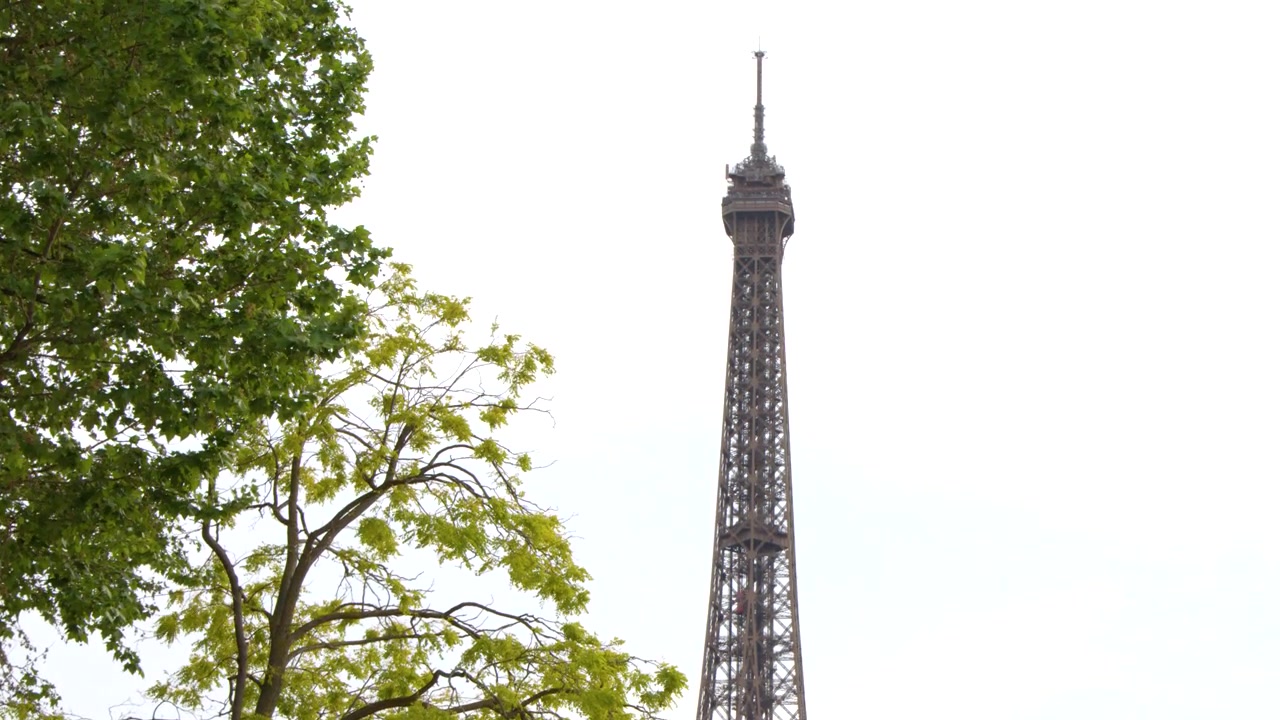 Inquadratura media statica della cima dell'iconica torre di ferro incorniciata da rigogliosi rami di alberi verdi.