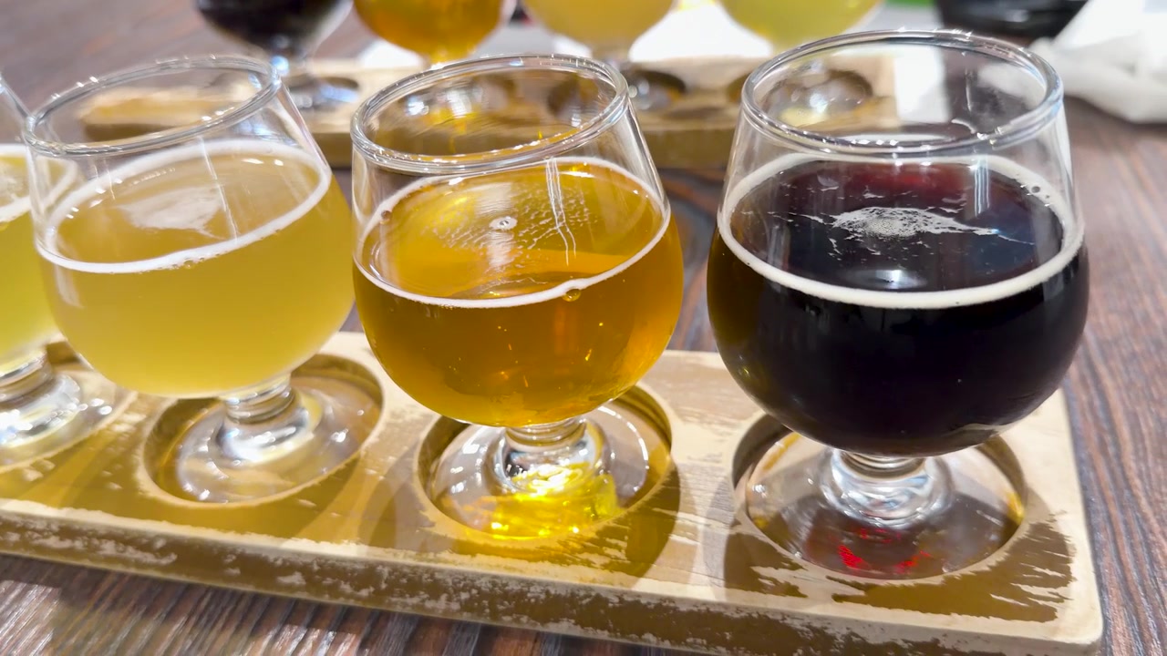 Tomada panorâmica em close-up de diversas cervejas artesanais em copos sobre uma tábua de degustação de madeira