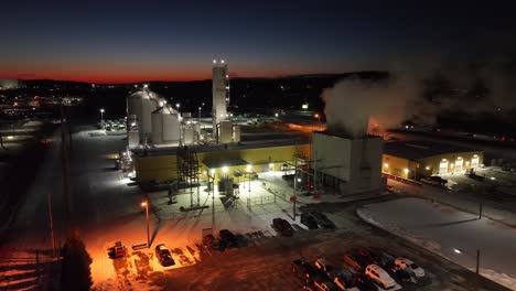 aerial view of an industrial facility at night with steam and lights, under a colorful sunset sky in the usa