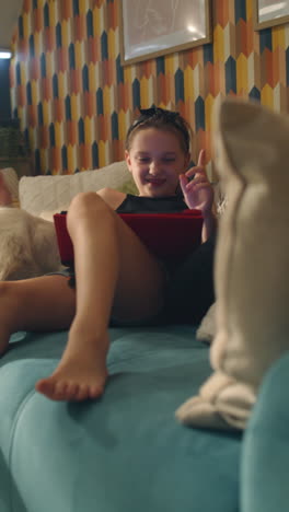 girl relaxing on a couch with a dog, watching a tablet