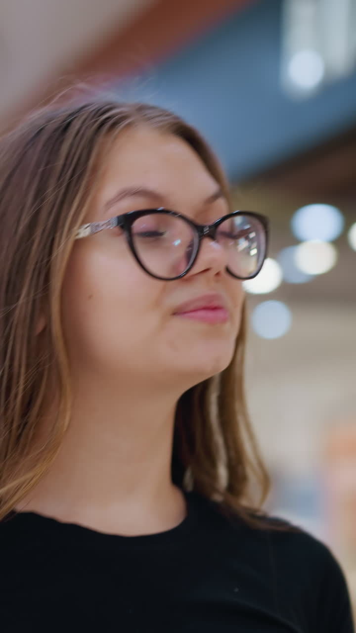 joven con camiseta negra y gafas mirando contemplativa con luces borrosas y estructuras indistintas en el fondo, creando una atmósfera reflexiva y reflexiva