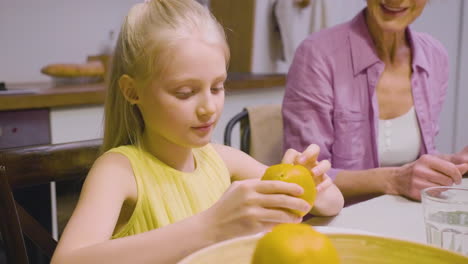 Close-Up-View-Of-A-Blonde-Girl-Peeling-An-Orange-During-A-Family-Dinner