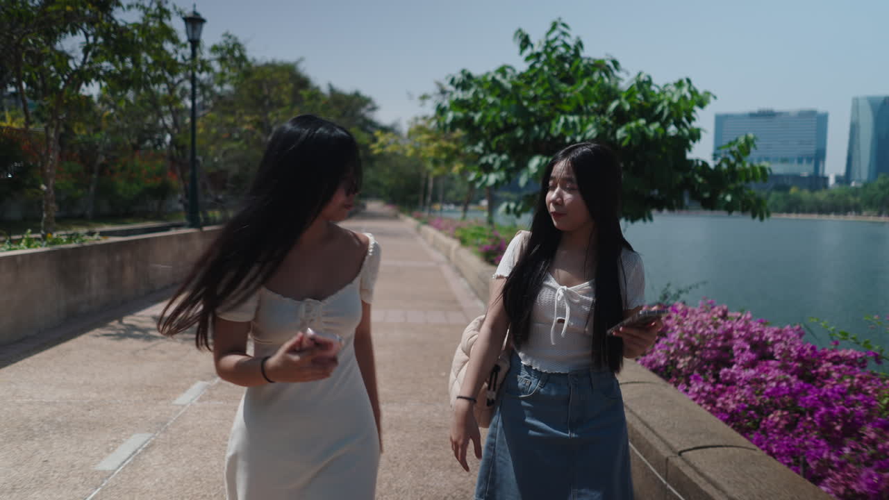 หญิงสาวสองคนเดินเล่นและแชทในสวนสาธารณะที่มีแดดสดใส