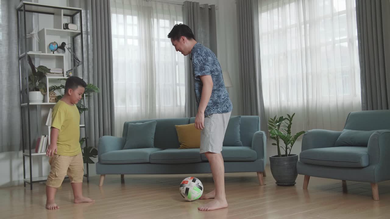 Happy Asian Father And His Son Playing Soccer In Living Room