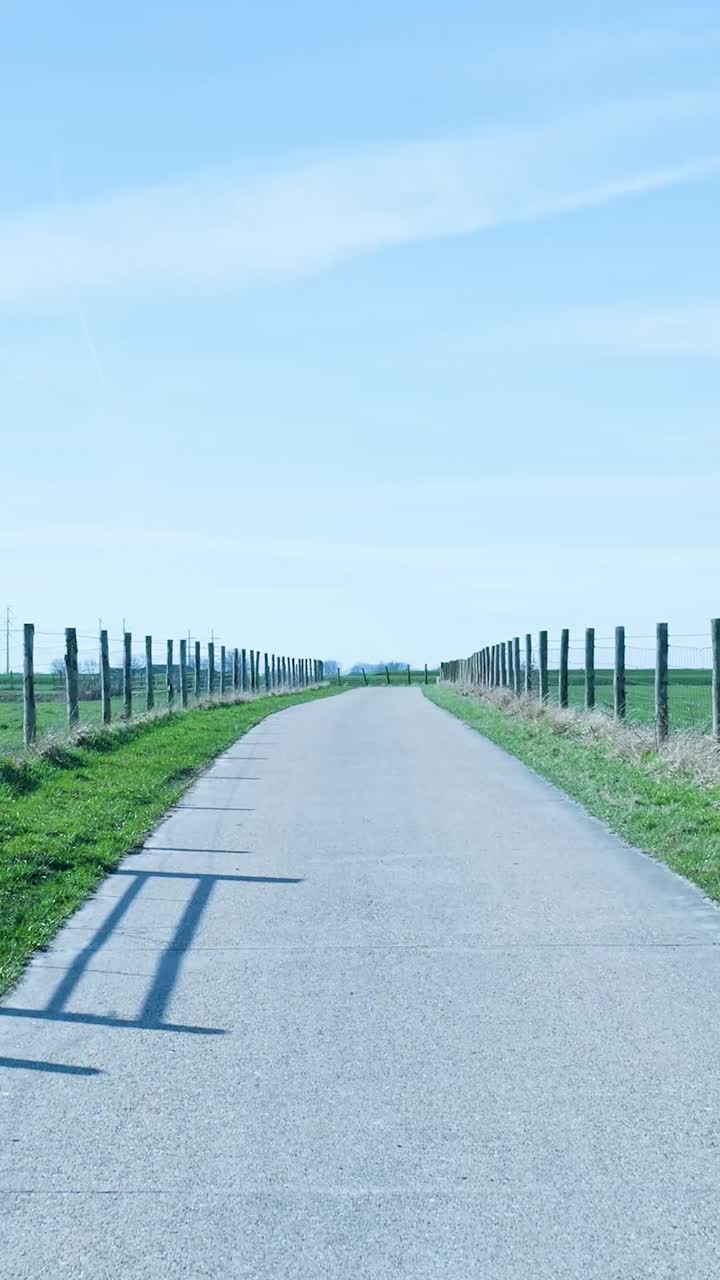 Largo camino de concreto en el campo con campos verdes y cielo azul.