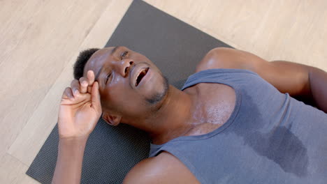 tired and sweaty african american man lying on exercise mat in sunny living room, slow motion